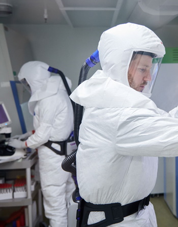 Two people in a lab wearing PPE and working